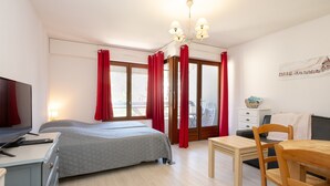 Une chambre à coucher avec un lit, un bureau, une chaise, une télévision et une fenêtre avec des rideaux.