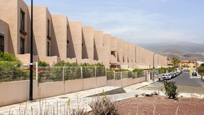 Un bâtiment moderne à la façade uniforme, une rue bordée de voitures garées et un ciel dégagé.