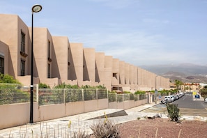A modern building with a uniform facade, a street with parked cars, and a clear sky.