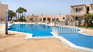 Une piscine entourée de bâtiments dotés de balcons, avec des chaises longues et des palmiers.