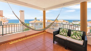 A balcony with a hammock, a wicker sofa with cushions, and a view of the sea and buildings. - Villa 'Kethellen' with Sea View, Private Terrace and Wi-Fi (Porto Covo)
