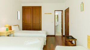 A hotel room with two beds, a wooden wardrobe, a small table with a lamp, and a mirror. - Villa 'Kethellen' with Sea View, Private Terrace and Wi-Fi (Porto Covo)