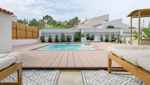 Un jardin avec une piscine, une terrasse en bois et du mobilier d’extérieur.