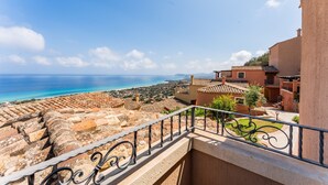 A balcony with a view of the sea, terracotta rooftops, and a clear sky.