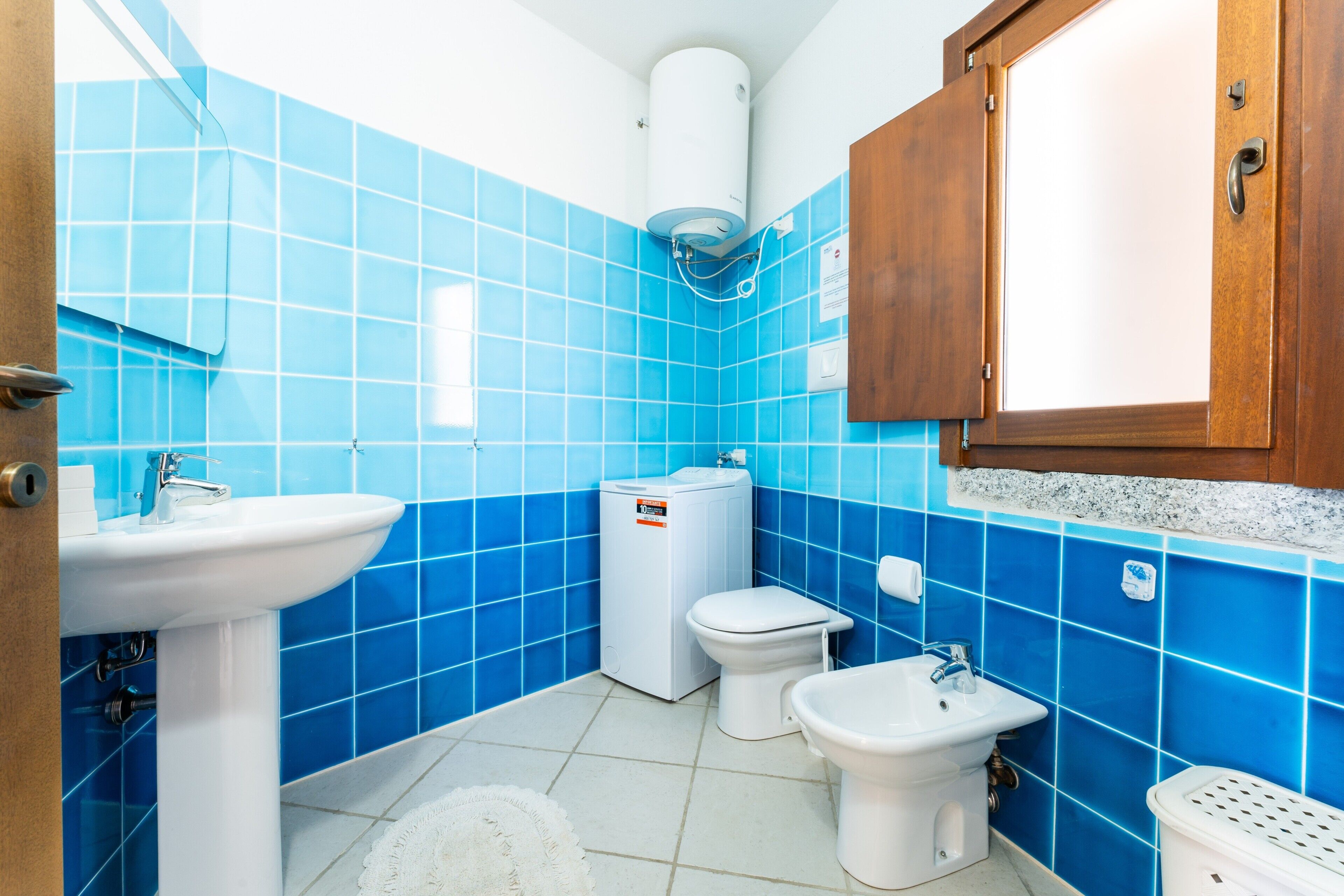 Un baño con azulejos azules, un lavamanos blanco, un inodoro, un bidé y un armario.