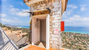 A stone building with a balcony, a view of the sea, and a sign indicating a fire extinguisher.