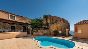 A swimming pool with a stone wall and a view of the sea.