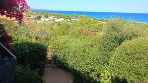 A garden pathway leading to a view of the sea, with lush greenery and a clear sky.