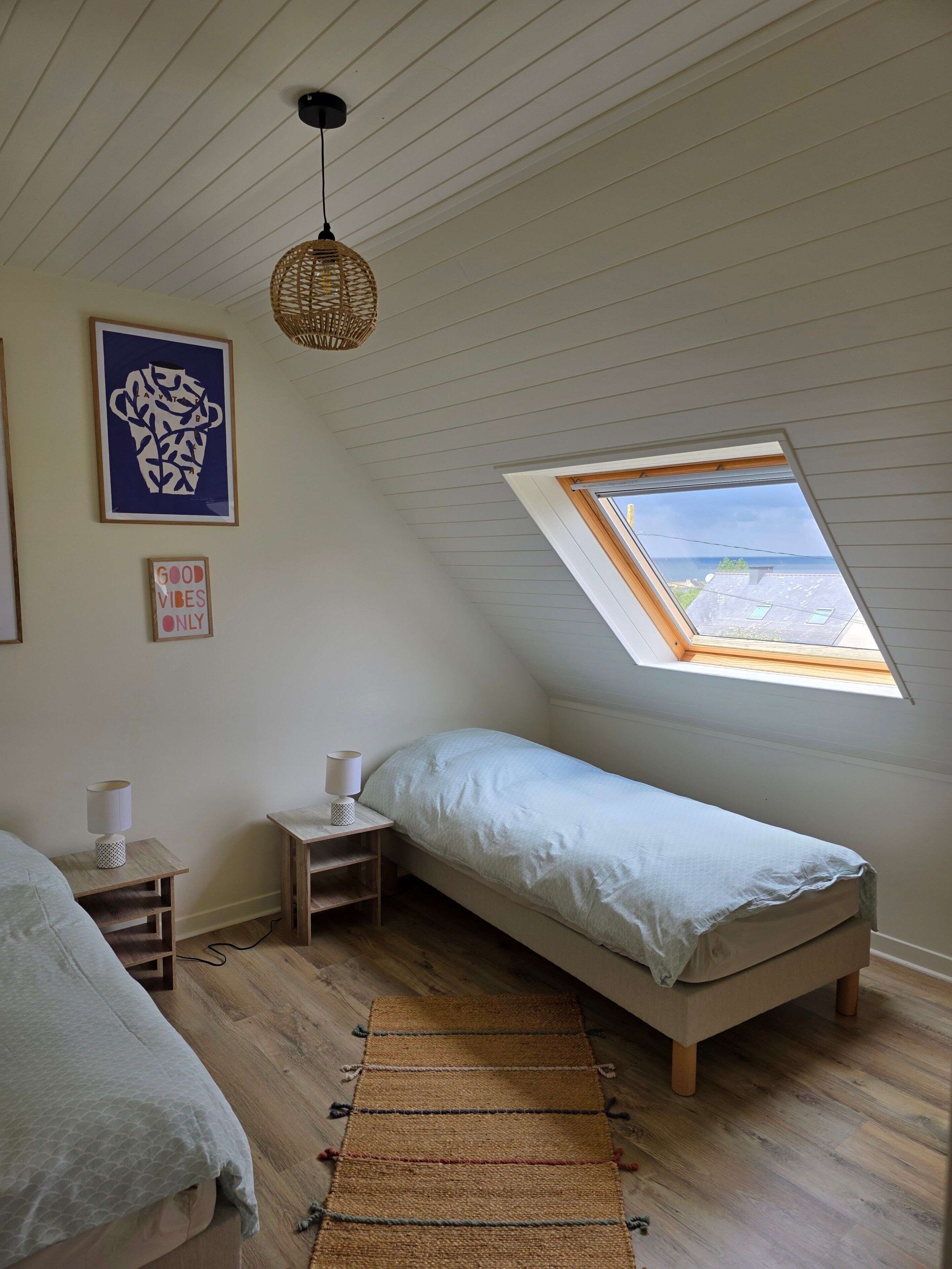 A bedroom with a skylight, a bed, a nightstand, a lamp, and a wall art piece.