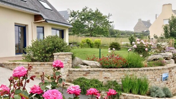 Ein Haus mit einer Steinsäule, einem Rosengarten und einem Holzzaun.