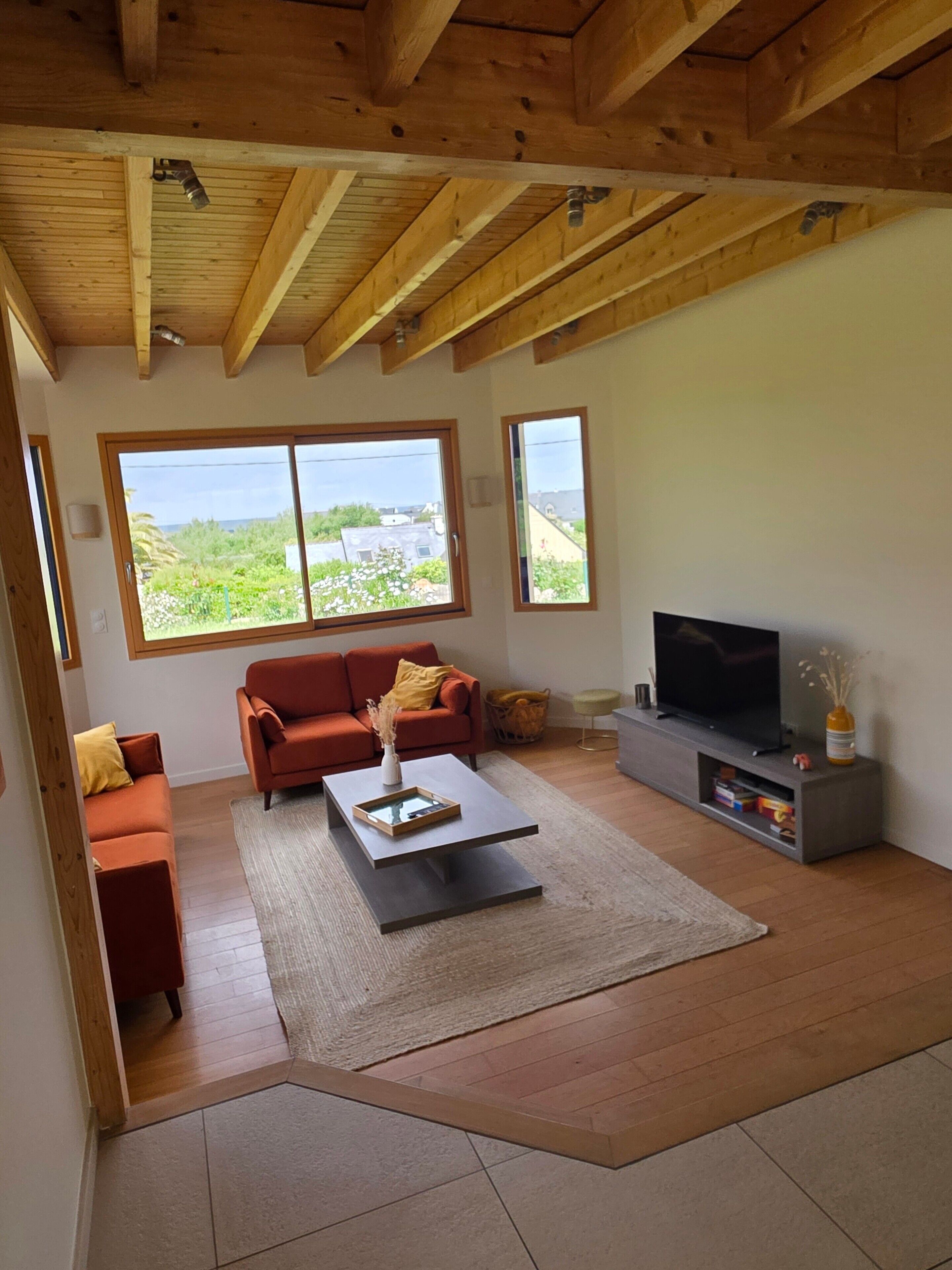 A living room with a wooden ceiling, a sofa, a coffee table, a TV, and large windows.