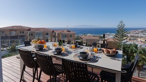 Une table à manger dressée pour le petit-déjeuner, avec vue sur l’océan et le paysage urbain.