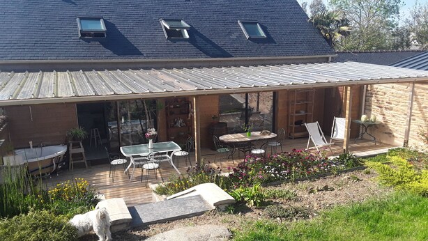 Une terrasse couverte avec des meubles d’extérieur, un petit jardin et un chien.