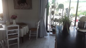 Un coin repas comprenant une table, des chaises, un vase de fleurs, un tableau accroché au mur et une plante en pot posée sur une étagère.