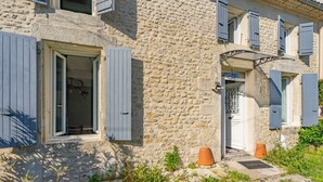 A stone building with a door, windows with shutters, and a small garden area with plants and a potted plant. - Holiday Home 'Maison À Cozes' with Private Terrace, Private Garden and Wi-Fi (cozes)