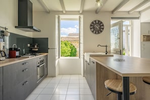 Uma cozinha moderna com uma ilha grande, forno embutido e vista através de uma porta aberta para o exterior.