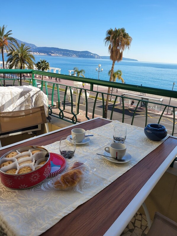 A table with pastries, cups, and a glass of water on a balcony overlooking a coastal view.