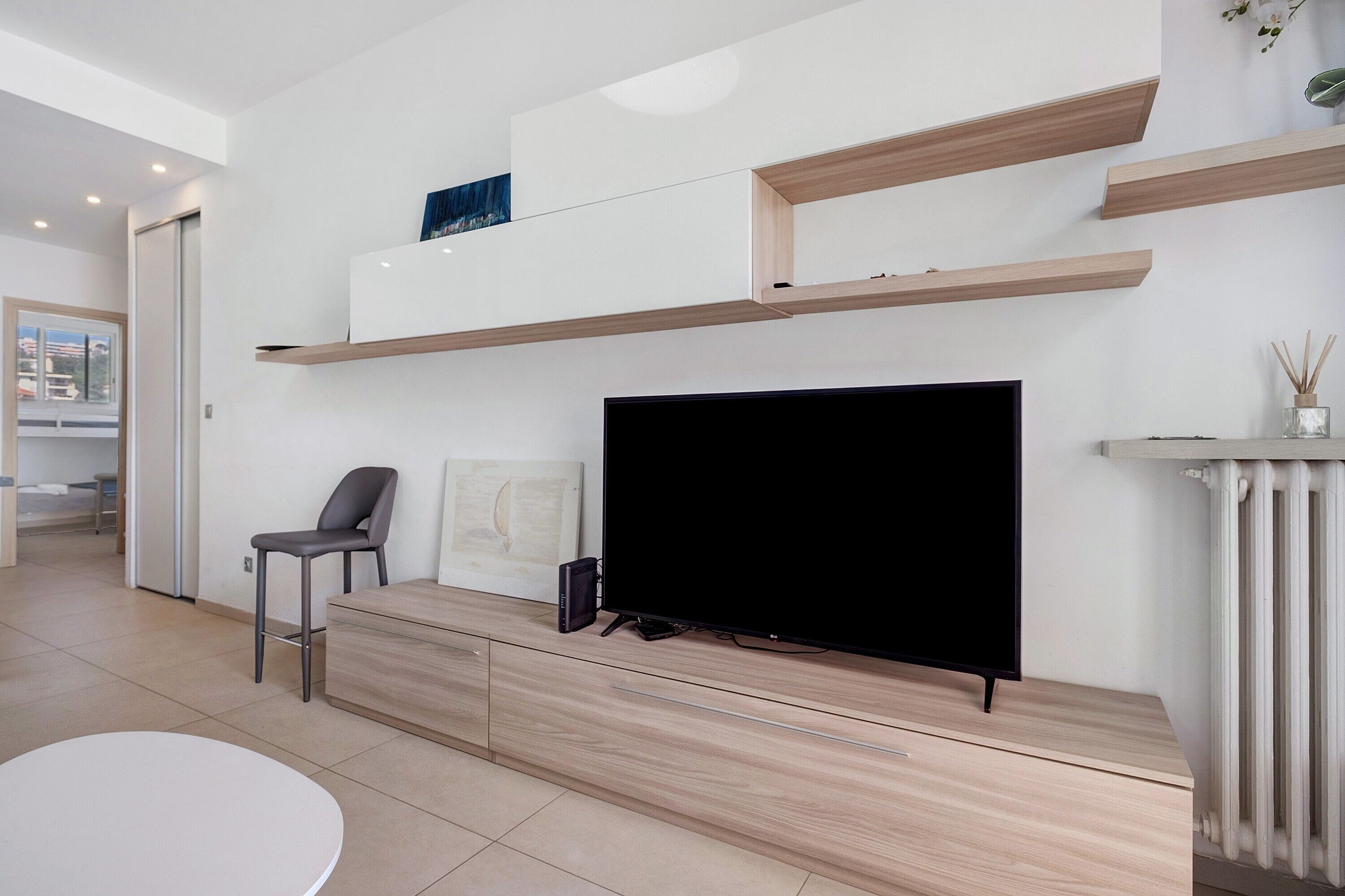 A modern living room with a flat-screen TV, wooden shelves, a chair, and a small table.