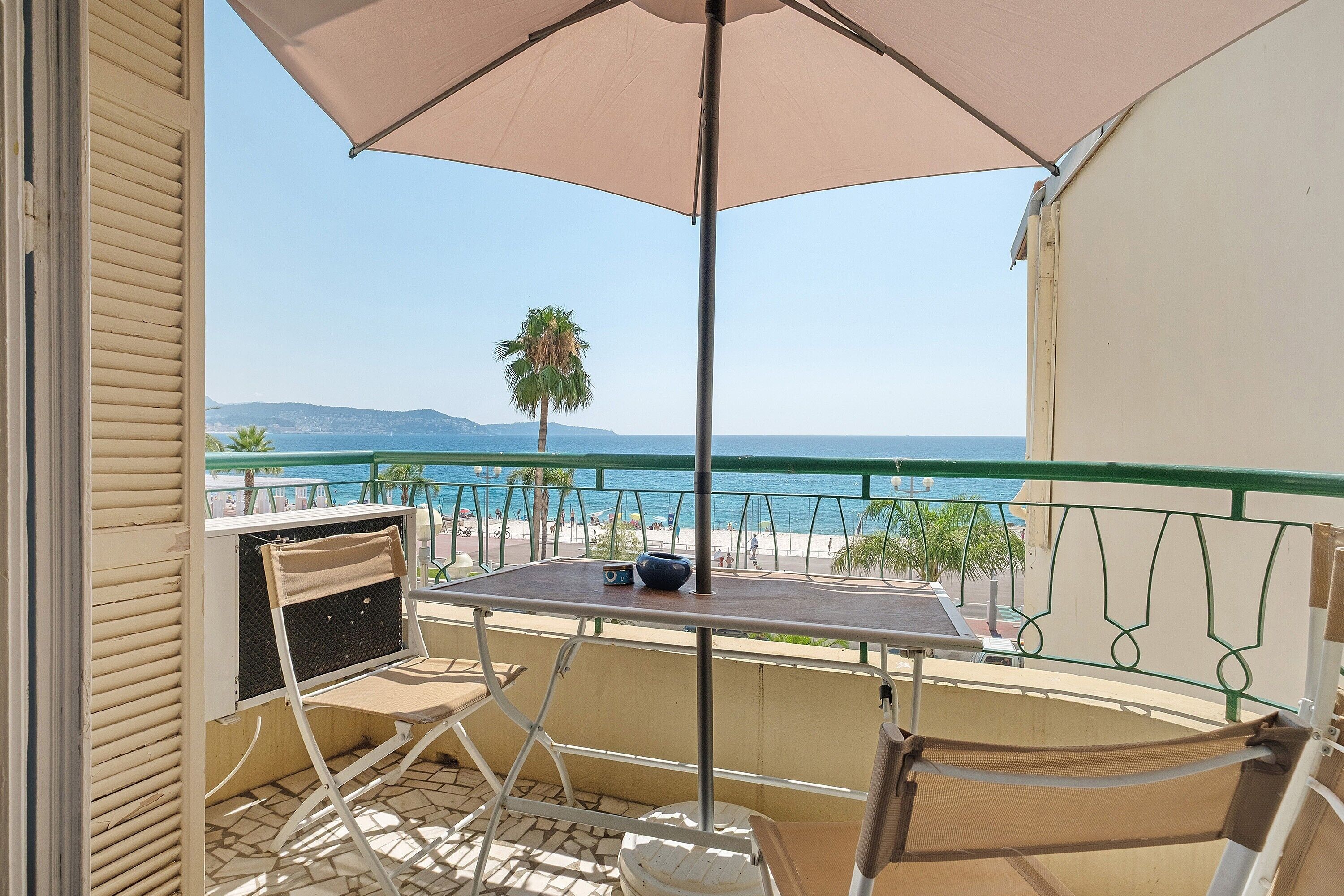 Un balcon avec une table et des chaises, donnant sur une plage et la mer.