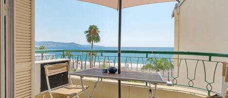 Un balcon avec une table et des chaises, donnant sur une plage et la mer.