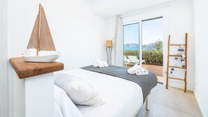 Un dormitorio moderno con una cama, un estante de madera con un modelo de velero, una escalera con adornos colgantes y vistas al exterior.