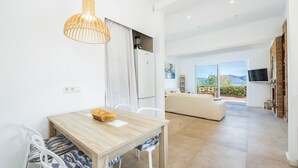Una cocina moderna con horno empotrado, un comedor con mesa de madera y sillas blancas, y una sala de estar con sofá y televisor.