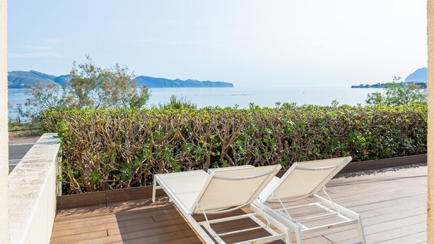 Una terraza con dos sillones blancos orientados hacia un cuerpo de agua y montañas distantes.