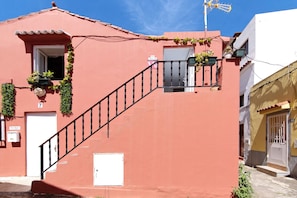 A building with a red facade, a staircase, a white door, and a window with plants.