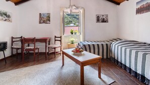 A cozy room with a wooden ceiling, a bed with striped bedding, a dining table with chairs, and a view of a green landscape through an open door. - Vacation Home 'Mi Idilio' with Mountain View and Wi-Fi (Teror)