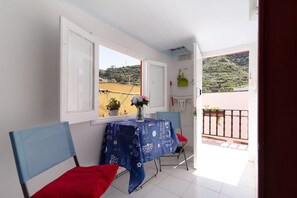 A balcony with a table and chairs, a window with a view of a hill, and a door.