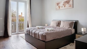 A bedroom with a bed, a world map on the wall, and a balcony with a view of a building.