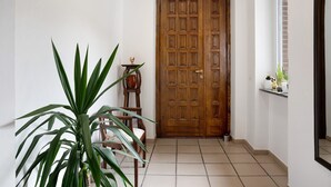 A hallway with a wooden door, a potted plant, a chair, and a window with a view.