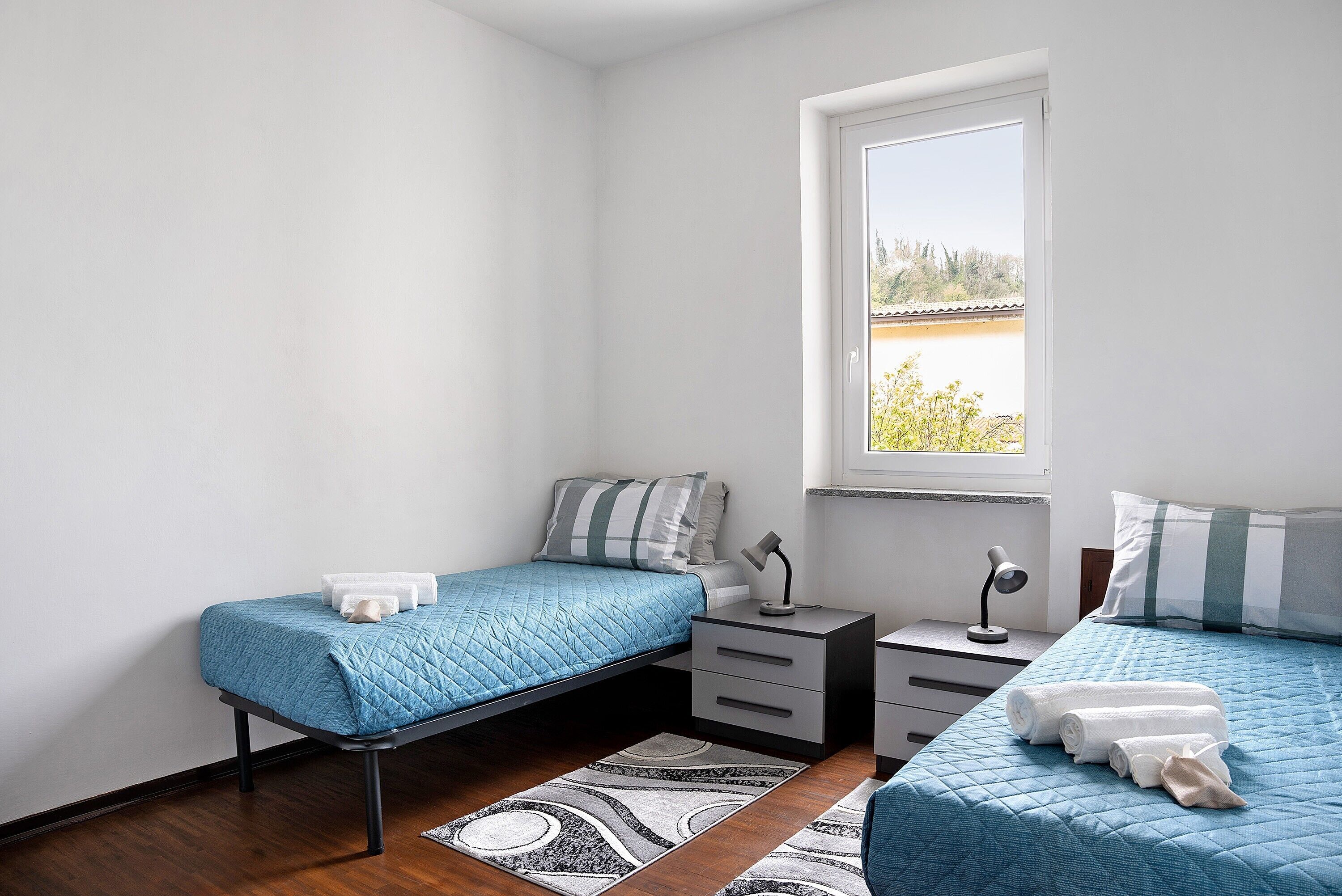 Un dormitorio con dos camas, una ventana, una mesita de noche y una mesita auxiliar.