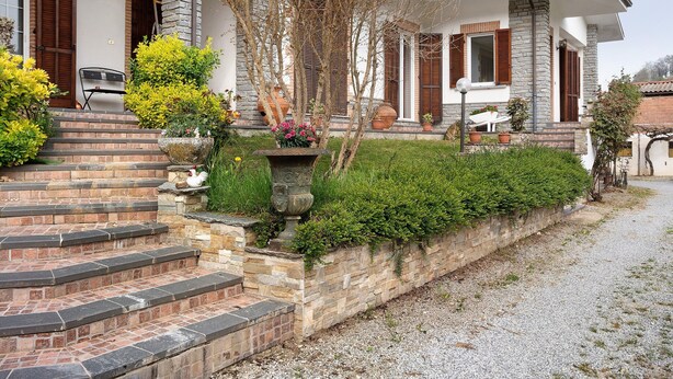 A house with stone steps leading to a door, a garden with various plants, and a gravel driveway.