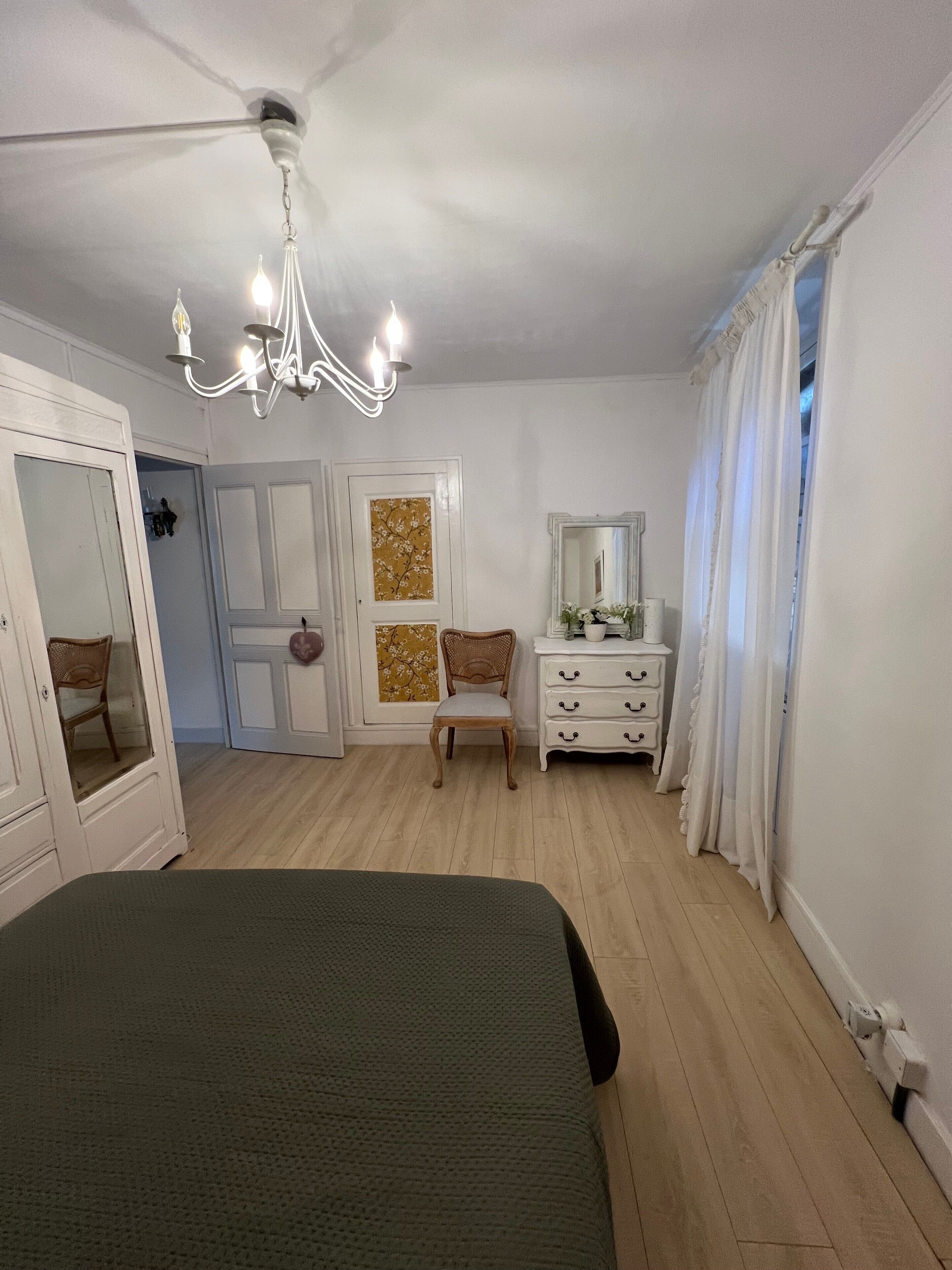 Ein Schlafzimmer mit Bett, Schminktisch, Stuhl, Spiegel und einer Chandelier.