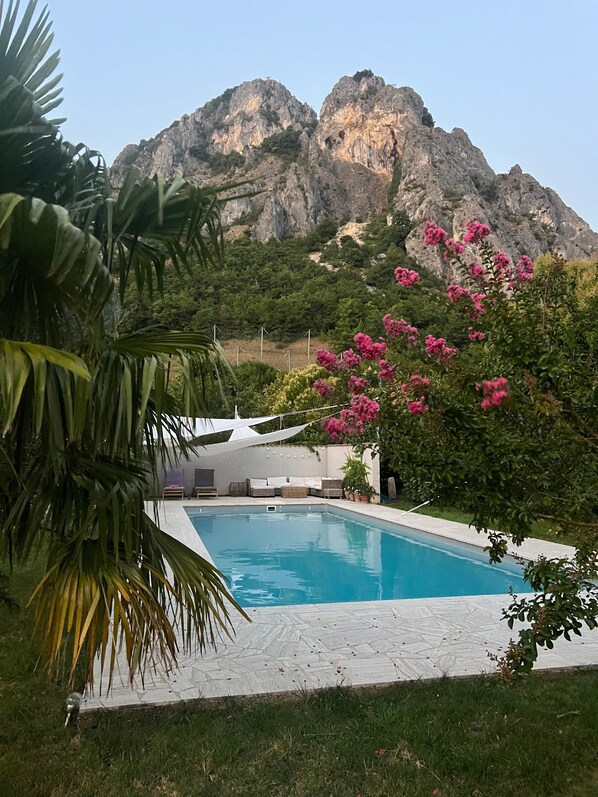 A swimming pool with a mountain backdrop, surrounded by greenery and potted plants.