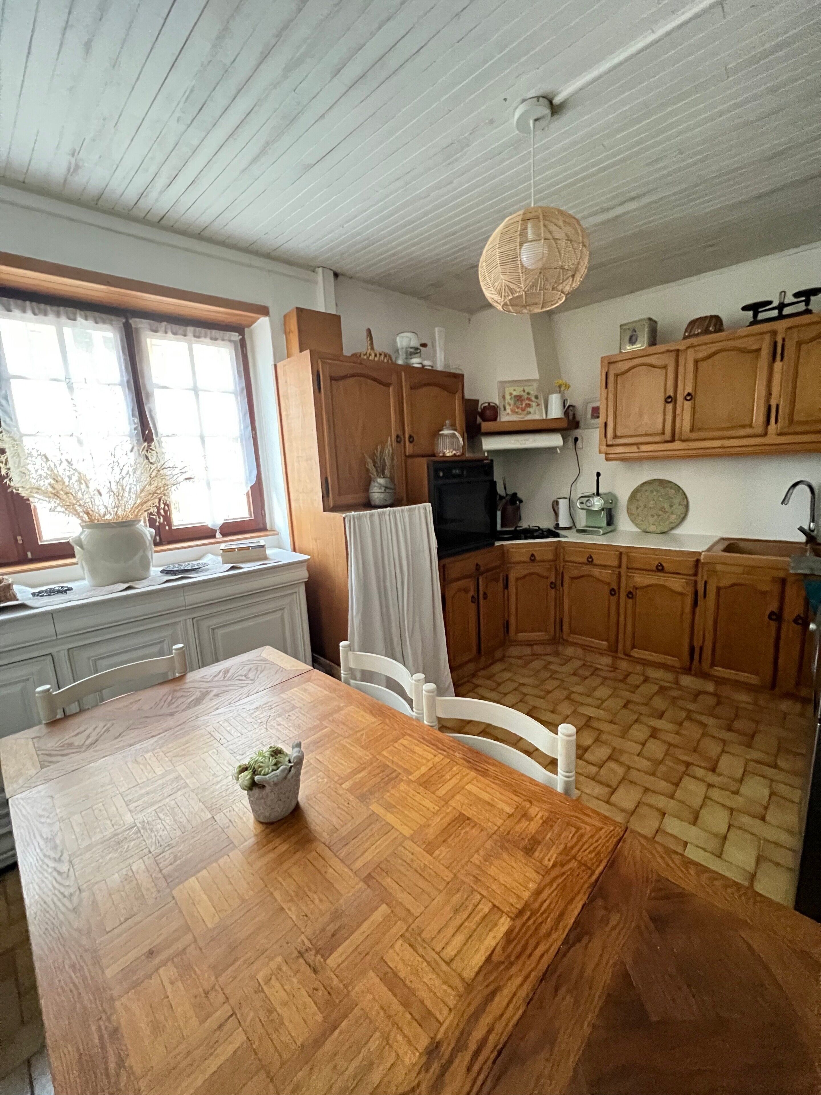 Ett kök med träskåp, ett matbord och en hängande lampa.