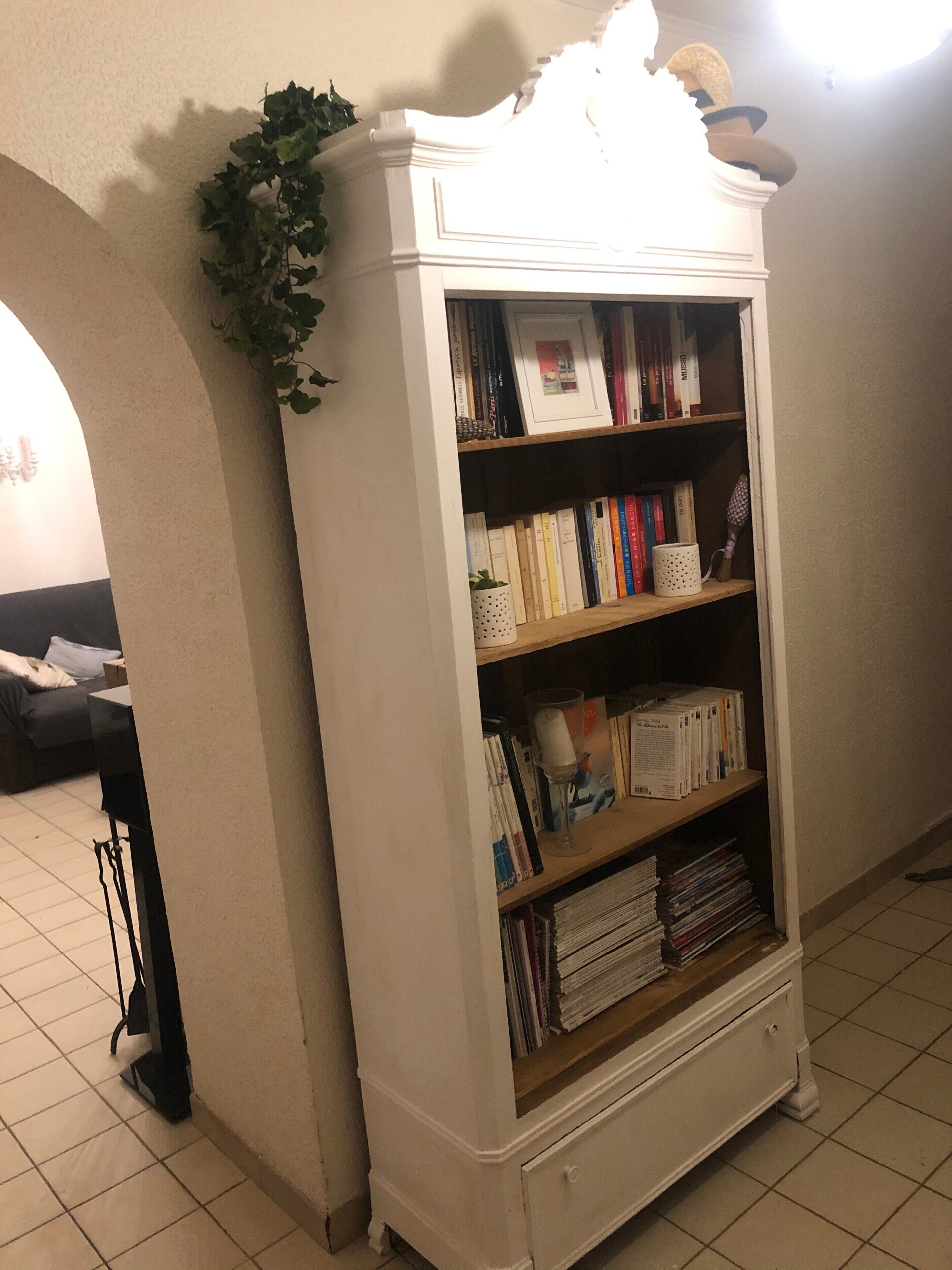 Een witte boekenkast met boeken en decoratieve items, een kamerplant en een betegelde vloer.
