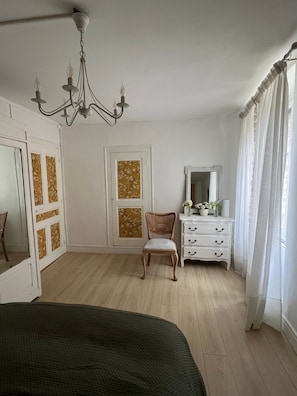 A bedroom with a bed, a dresser, a chair, a mirror, and a chandelier.