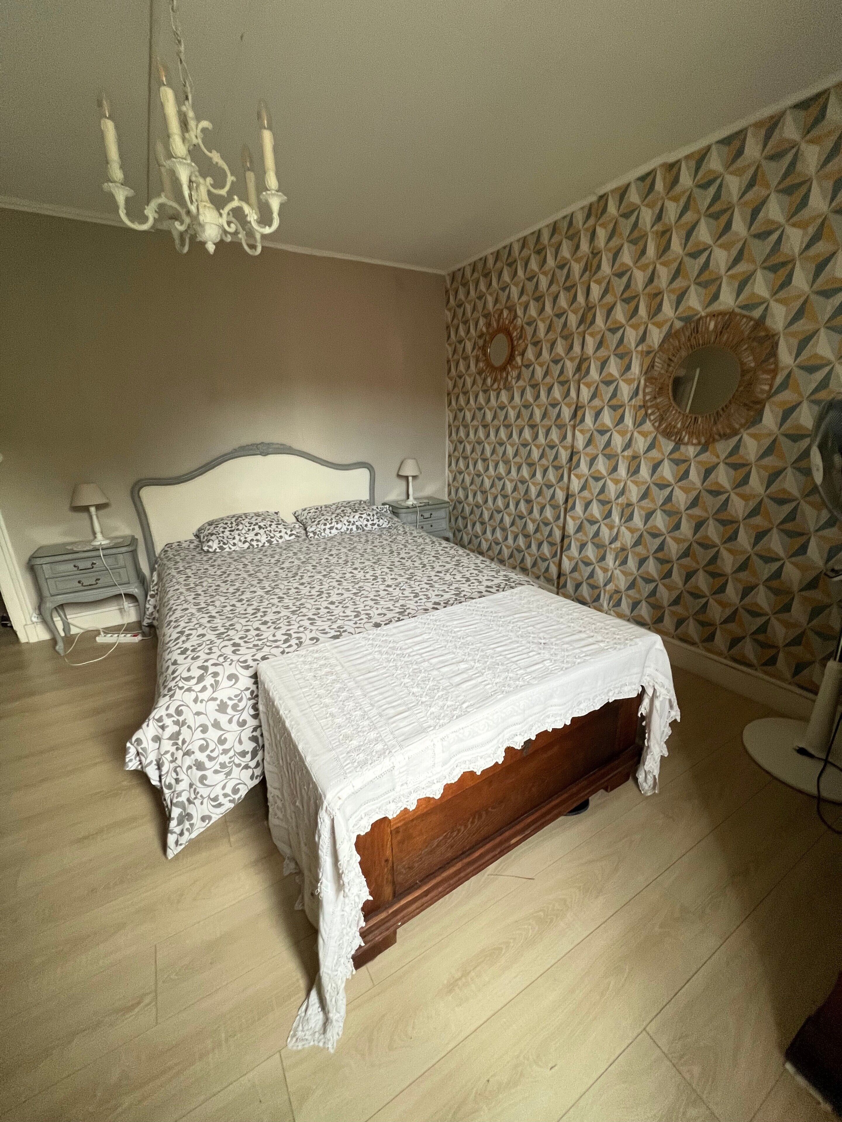 A bedroom with a wooden bed, patterned bedding, a chandelier, bedside lamps, and a geometric-patterned wall.