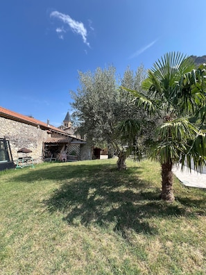 A stone building with a tiled roof, a palm tree, and a grassy yard.