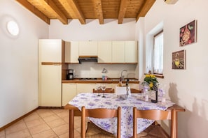 A kitchen with wooden cabinets, a dining table with a floral tablecloth, and a window with artwork. - Apartment 'Bilo Garden Agriturismo Teboi' with Shared Pool, Shared Terrace and Wi-Fi (Lazise)
