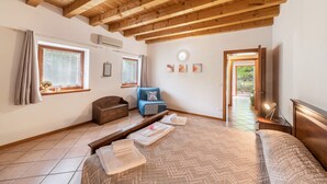 Een slaapkamer met een houten plafond, een bed met een gewatteerde spreideken, een blauwe bank, een houten kist en een raam met gordijnen.
