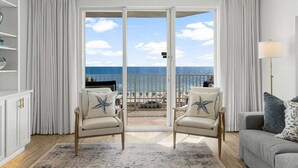 Una habitación con vista al océano, un balcón con mobiliario exterior y un sofá con almohadones decorativos.