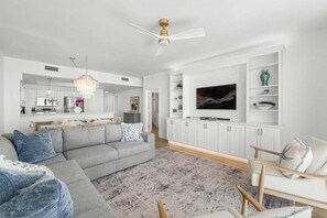 Una sala de estar moderna con un sofá gris, un mueble blanco para entretenimiento y un ventilador de techo.