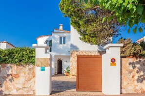 Un edificio bianco con un muro in pietra, un cancello in legno e un segnale che indica divieto di sosta.