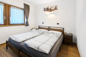 Un lit double avec une tête de lit en bois, une table de chevet avec une lampe, une fenêtre avec des rideaux et une œuvre d’art accrochée au mur.