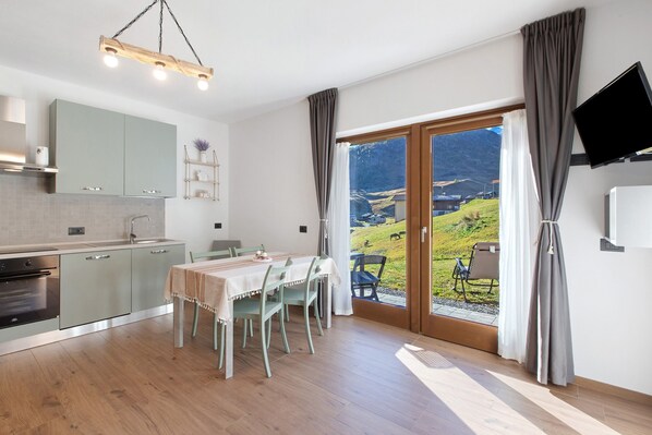 Une cuisine moderne avec un coin repas, un téléviseur fixé au mur et une vue sur l’extérieur.