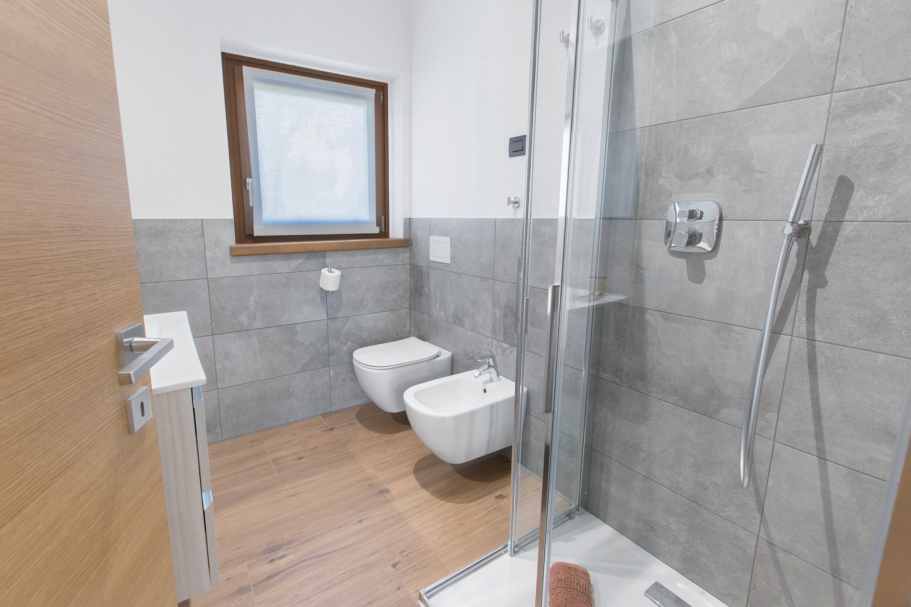 A modern bathroom with a glass shower enclosure, a toilet, and a bidet.