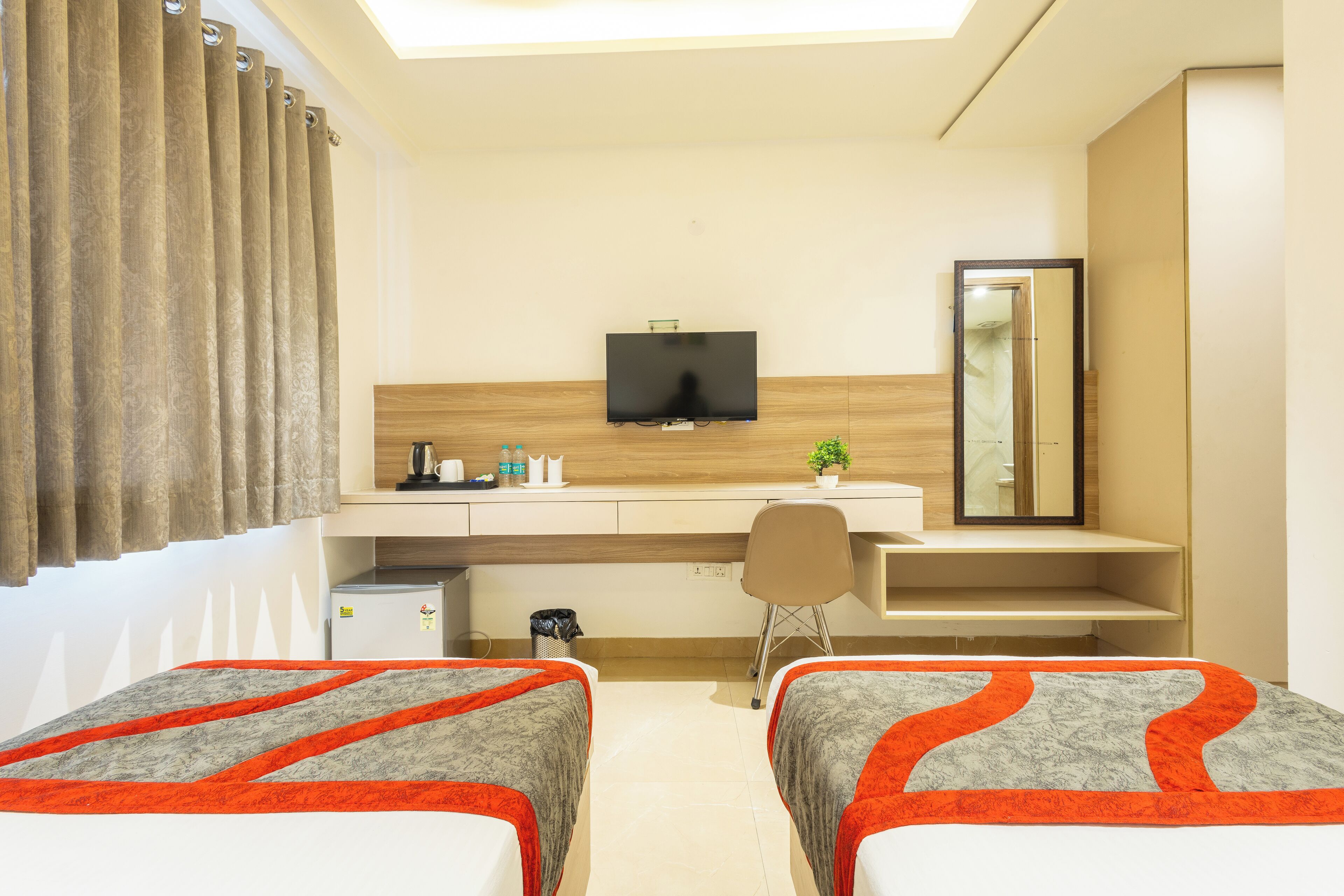 A hotel room with two beds, a desk, a television, and a mirror.